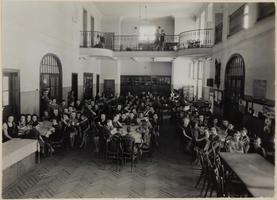 Children sitting at tables in a spacious room, looking toward the camera.