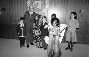 A man posing with a group of children, the United Nations logo on a wall behind them.