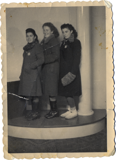 Three young women posing on a small, raised platform, wearing winter coats with Stars of David on them.
