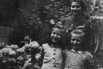 Coiffées de boucles, deux fillettes souriantes posent avec une femme dans un jardin en fleurs. Coiffées de boucles, deux fillettes souriantes posent avec une femme dans un jardin en fleurs.