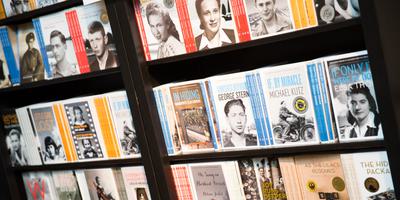 Books with black and white author portraits on their covers are neatly arranged on dark shelves. Some covers feature gold or silver award stickers. Titles and author names are visible but not clearly readable.