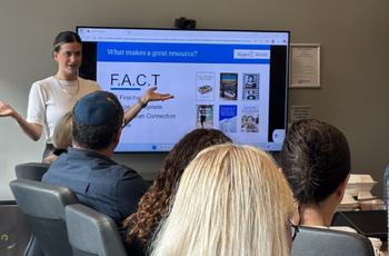A woman presents to a seated group, gesturing near a screen displaying a slide with books and F.A.C.T. acronym listed.